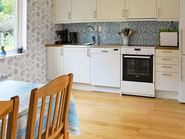 A kitchen with white cabinets, a Siemens dishwasher, a Siemens oven, a sink with a faucet, and a window with a view of greenery.