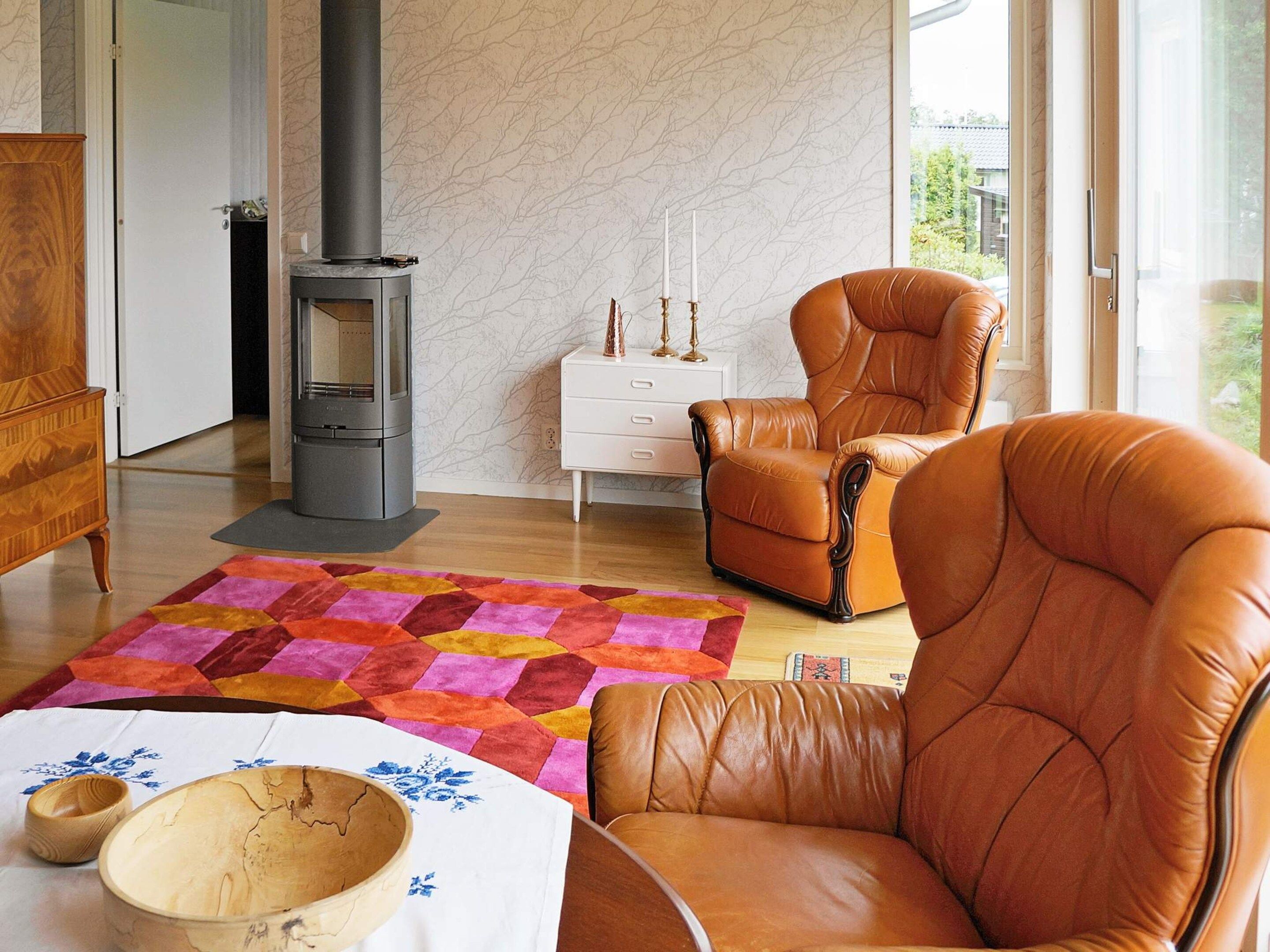 Una sala de estar con chimenea, sillones de cuero, un tapete colorido y una mesa de madera con cuencos.