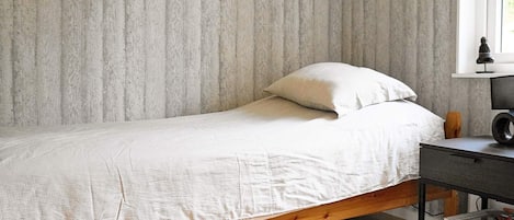 A single bed with a wooden frame, a white mattress, and a pillow against a textured wall.