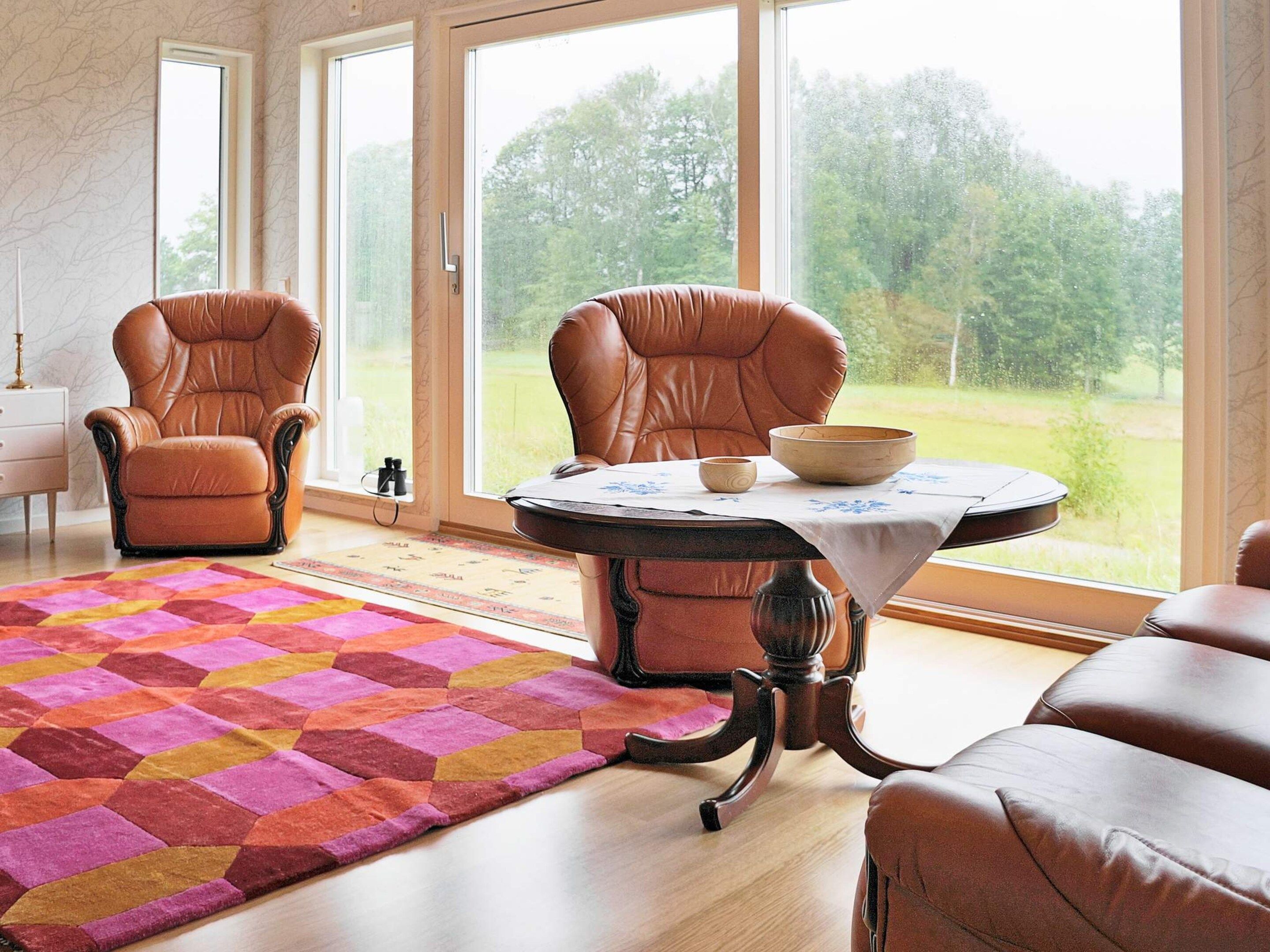 A room with two leather chairs, a round table with a bowl, and a colorful rug.