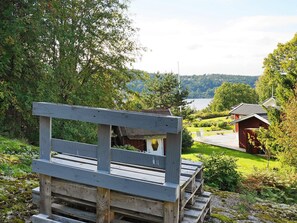 A wooden bench overlooking a lake with a red building in the background. - Holiday Home in Ljungskile (Ljungskile)
