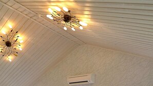 A room with a sloped ceiling, a decorative light fixture, an air conditioning unit, and large windows with a view of trees. - Holiday Home in Ljungskile (Ljungskile)