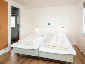 Una habitación con dos camas individuales, suelo de madera, pared blanca y un estante con una bandera.