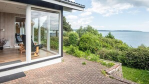 A modern house with a glass door leading to a patio with outdoor furniture. - 4 Person Holiday Home in Borkop (Borkop)