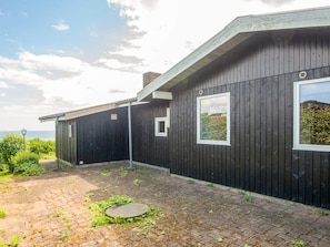 A modern building with a dark exterior, a brick pathway, and a view of the sea. - 4 Person Holiday Home in Borkop (Borkop)