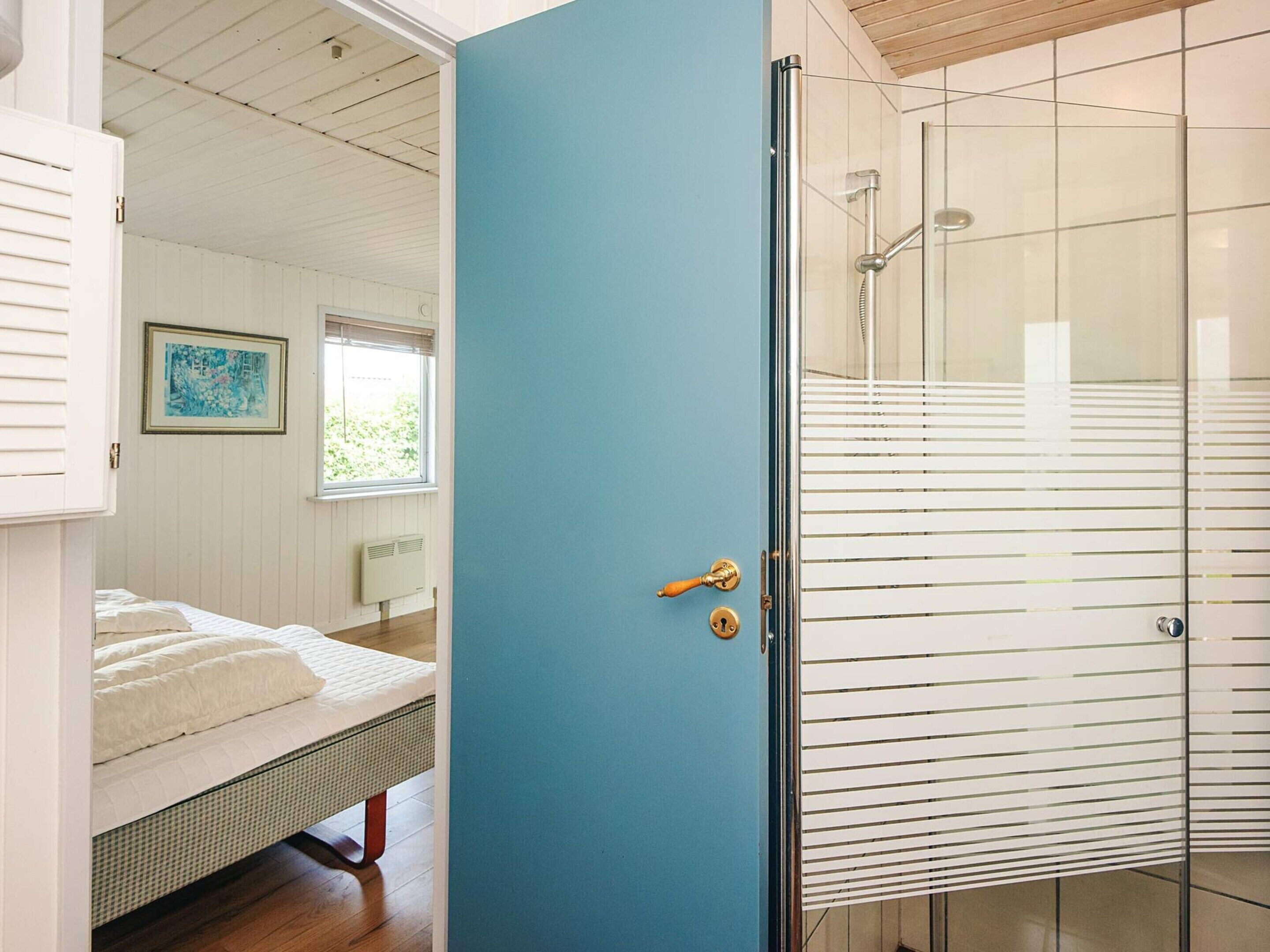 A room with a bed, a blue door, and a glass shower enclosure.