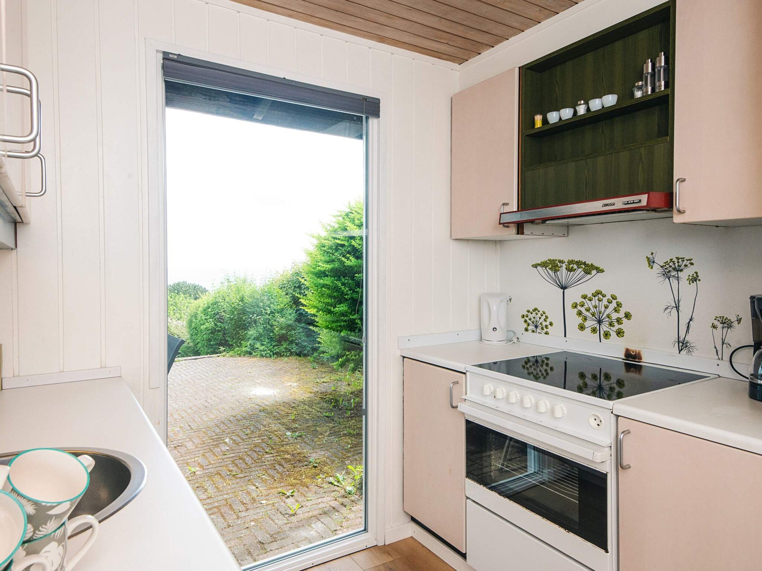 A kitchen with a built-in oven, a coffee maker, and a window overlooking a garden.