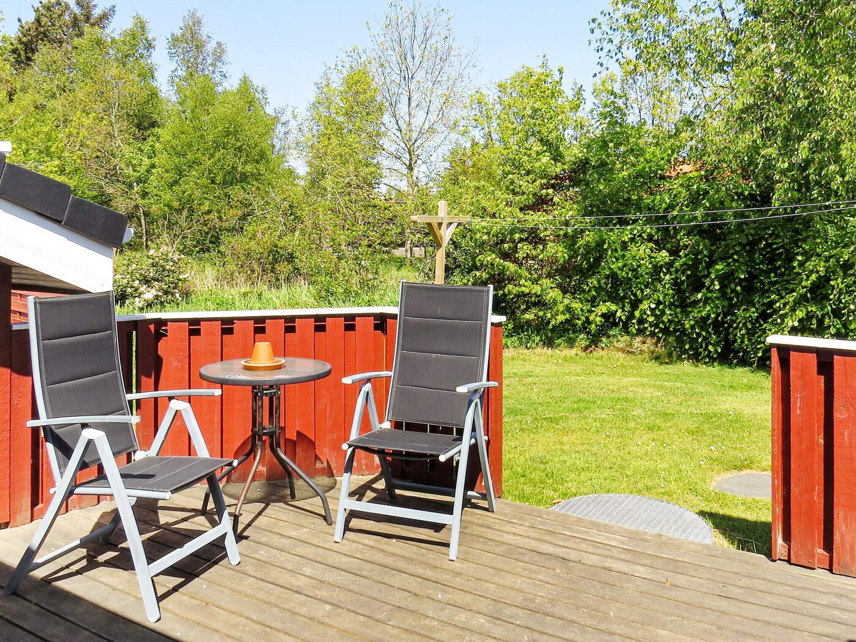 An outdoor patio area with two chairs and a small round table, surrounded by a wooden deck and a red fence.