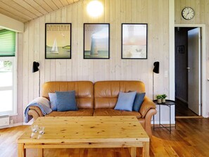 Um quarto com sofá de couro marrom, duas quadros com paisagens dinamarquesas, uma mesa de centro de madeira e uma mesinha lateral com plantas.