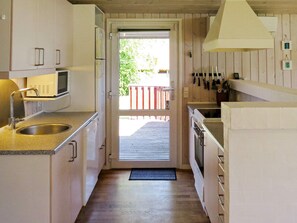 Cozinha pequena com piso de madeira, micro-ondas, pia e porta para área externa.