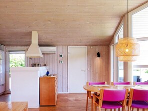 A room with wooden walls and ceiling, a white door, a wooden table with purple chairs, and a hanging light fixture. - Cozy Holiday Home in Jutland near Beach (Hals)