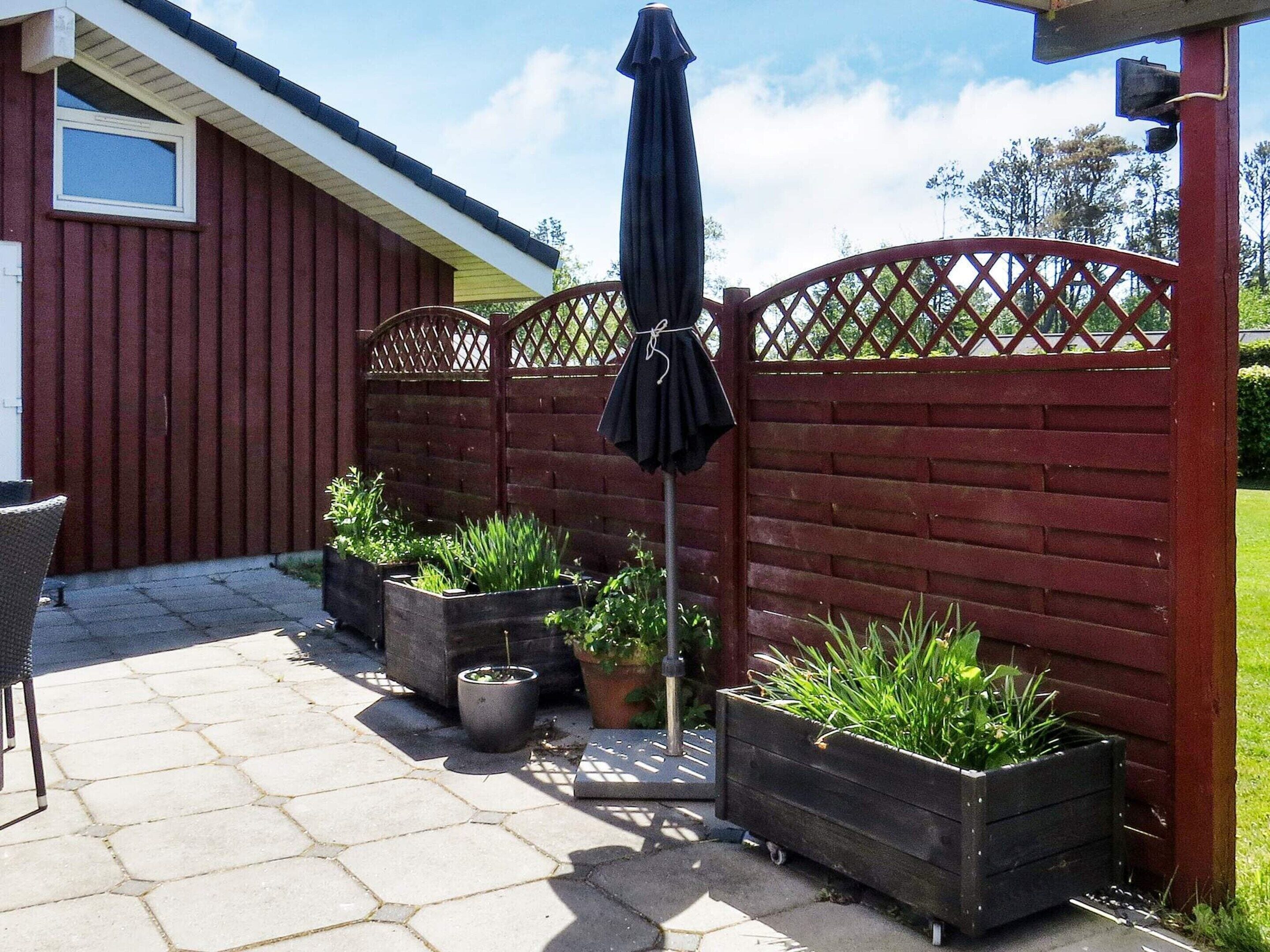 A patio area with a red fence, potted plants, a chair, and an umbrella.