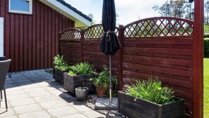 A patio area with a red fence, potted plants, a chair, and an umbrella. - Cozy Holiday Home in Jutland near Beach (Hals)