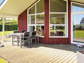 A covered outdoor area with a table and chairs, a large window, and a view of a garden. - Cozy Holiday Home in Jutland near Beach (Hals)