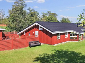 A red barn-style building with a sloped roof, a fenced area, and a bench.