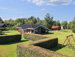 A modern house with a covered patio and a swing set in a well-maintained garden. - Cozy Holiday Home in Jutland near Beach (Hals)
