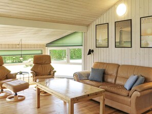 A room with a wooden ceiling, a brown leather sofa, a wooden coffee table, and a green-framed window.