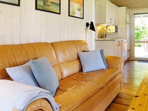 A tan leather sofa with two cushions, a wooden floor, and a kitchen area with a microwave and cabinets. - Cozy Holiday Home in Jutland near Beach (Hals)