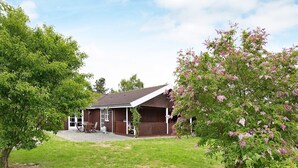A single-story house with a covered porch, a lawn, and a tree with pink flowers.