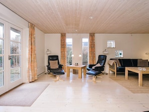 A spacious living area with a wooden ceiling, large windows, and a black leather sofa.
