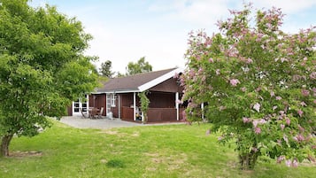 Uma casa com varanda, gramado e uma árvore com flores cor-de-rosa.