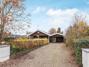 A single-story building with a sloped roof, a satellite dish, and a gravel driveway leading to a garage.