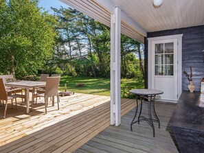 A wooden deck with a table and chairs, a small round table, and a door leading to a covered area.