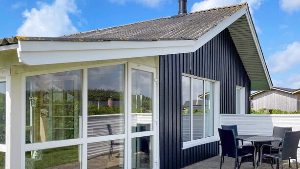 Una casa moderna con un amplio ventanal y ventanas, un patio con mesa y sillas, y una chimenea.