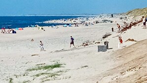 A beach with people walking and sitting, tents, and a clear sky. - 5 Person Holiday Home in Ringkobing-by Traum (Ringkobing)