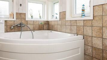 Un baño con una bañera grande, tres ventanas y un revestimiento de azulejos.