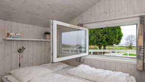 Un dormitorio con una cama, una ventana, una estantería con libros y una planta en maceta.
