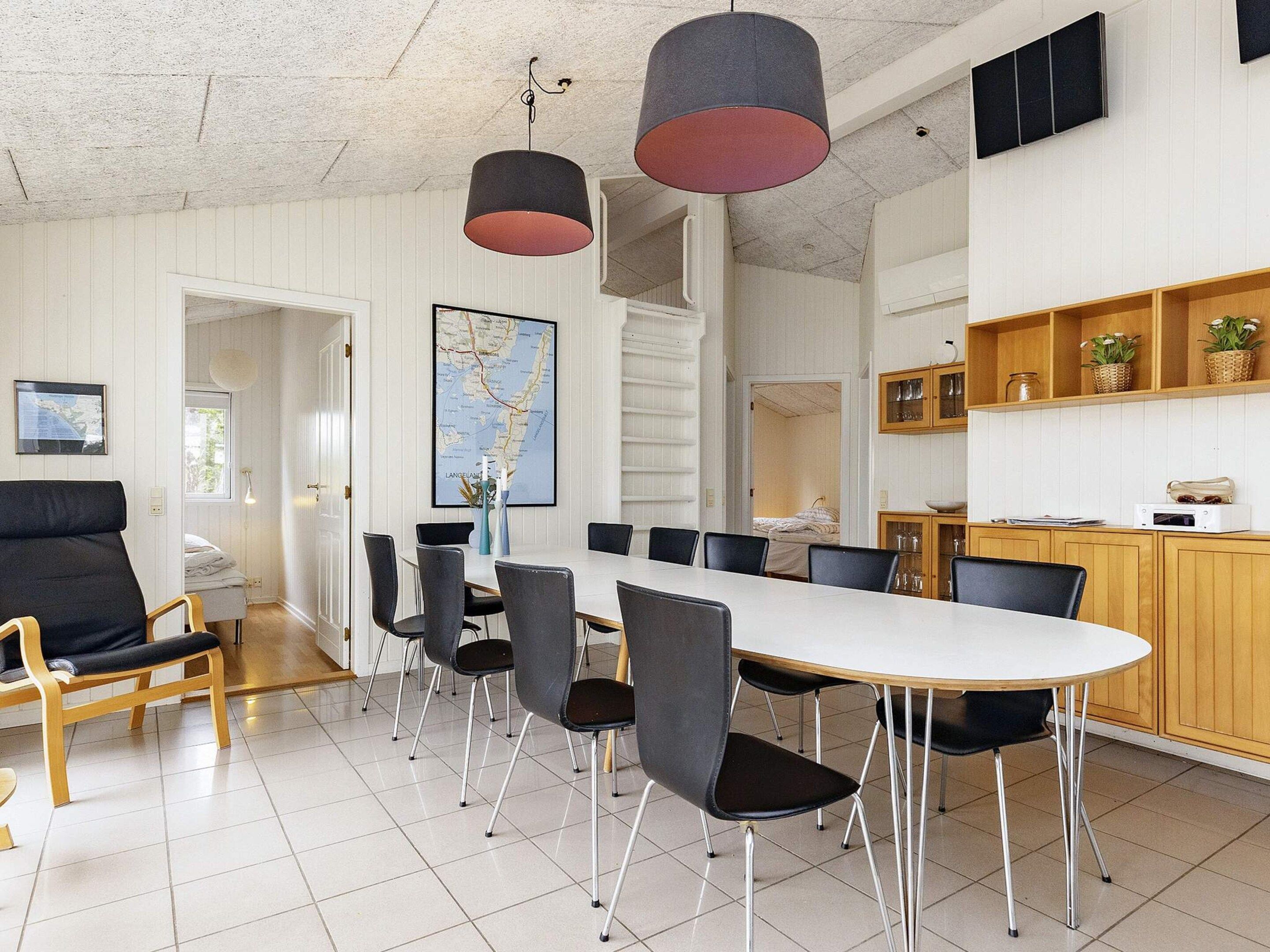 A modern dining area with a long table, multiple chairs, and pendant lighting.