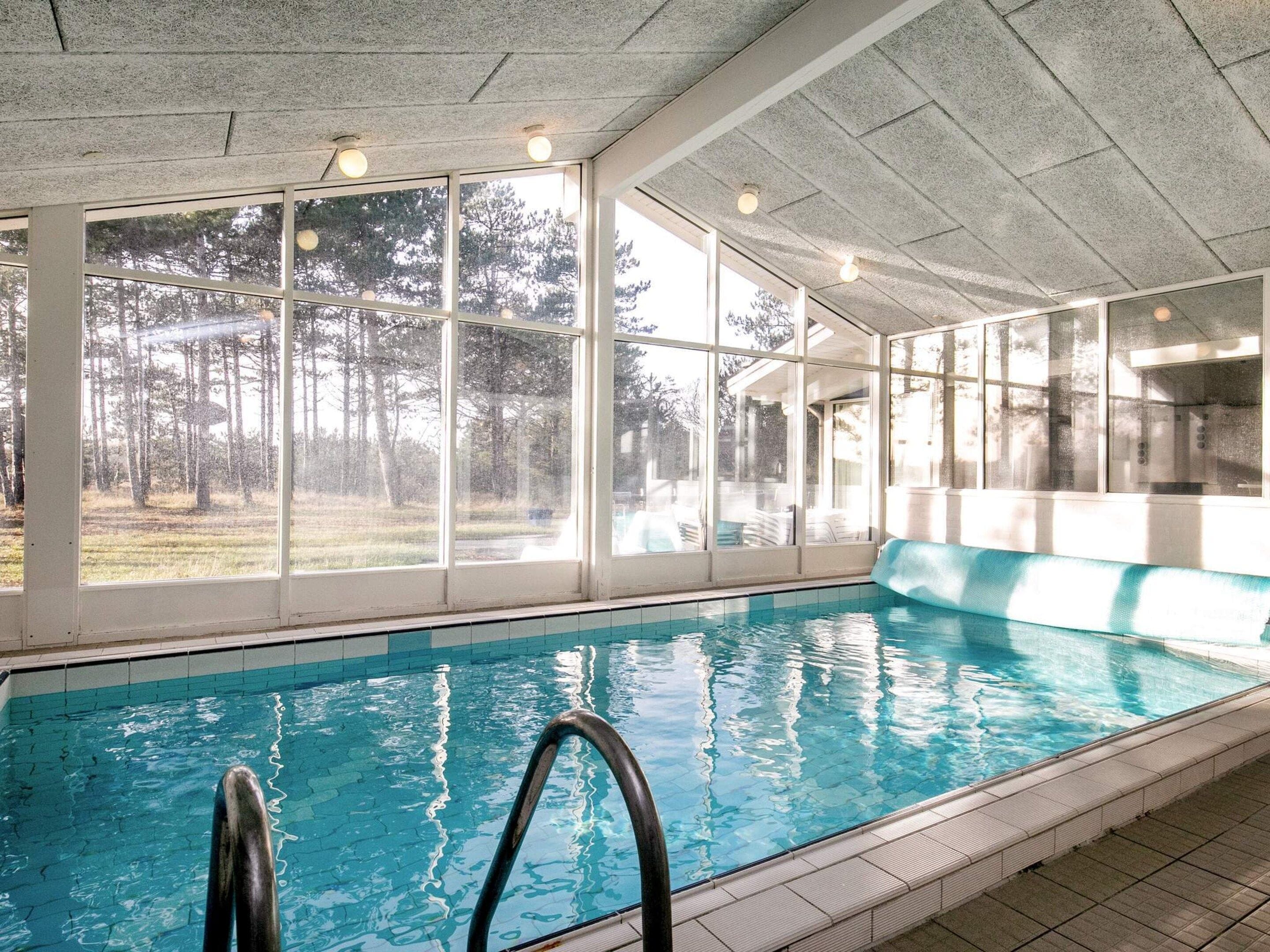 An indoor swimming pool with clear glass walls, a tiled floor, and a pool ladder.