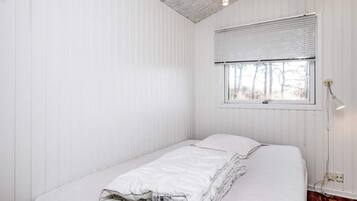 A small, white, single-bed room with a window and a ceiling light fixture.