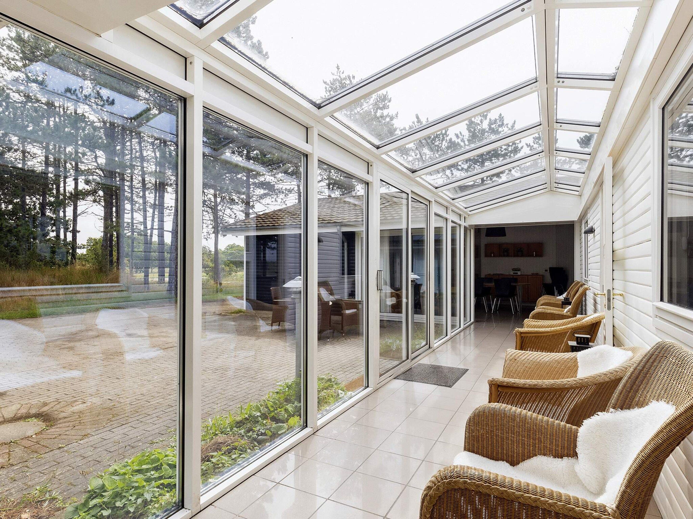 A covered patio with glass walls, wicker furniture, and a view of the outdoors.