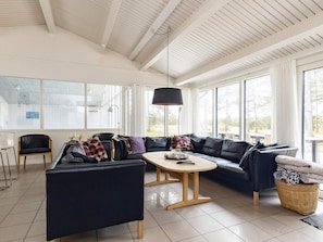 A modern living room with a black leather sofa, a wooden coffee table, and a large window providing natural light. - 16 Person Holiday Home in Humble (Sydlangeland)