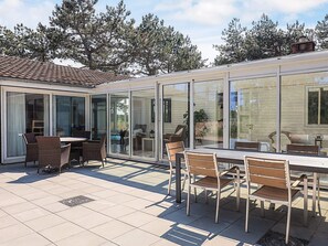 A covered patio with a table and chairs, a sliding glass door, and a view of a pool and trees. - 16 Person Holiday Home in Humble (Sydlangeland)