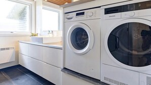 Ein moderner Waschraum mit zwei Waschmaschinen mit Frontlader, einem Waschbecken und einem Fenster.
