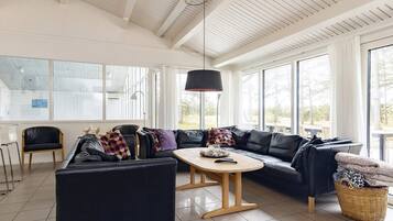 A modern living room with a black leather sofa, a wooden coffee table, and a large window providing natural light.
