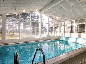 Une piscine intérieure avec des parois en verre transparent, un sol carrelé et un escalier d’accès à la piscine.