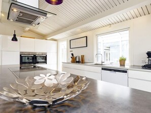 Une cuisine moderne avec des meubles blancs, des appareils en acier inoxydable et un grand îlot central agrémenté d’un saladier décoratif.
