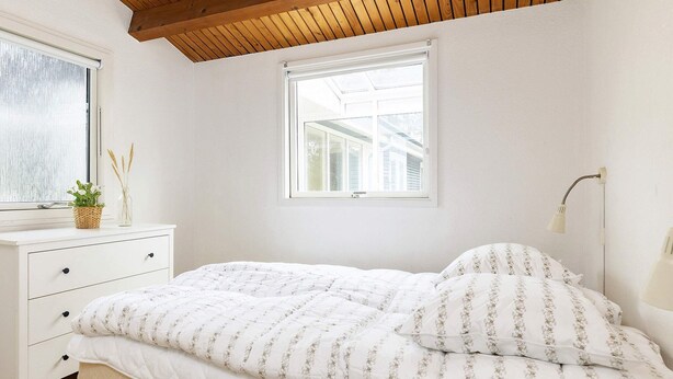 Ein Schlafzimmer mit Holzboden, einem weißen Bett mit Blumenbettwäsche, einem Nachttisch mit Lampe und einem Fenster mit Blick auf ein Haus.
