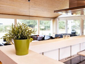A modern kitchen with a green plant on the counter, large windows, and a dining area with a sofa. - 5 Star Holiday Home in Saltum (Saltum)