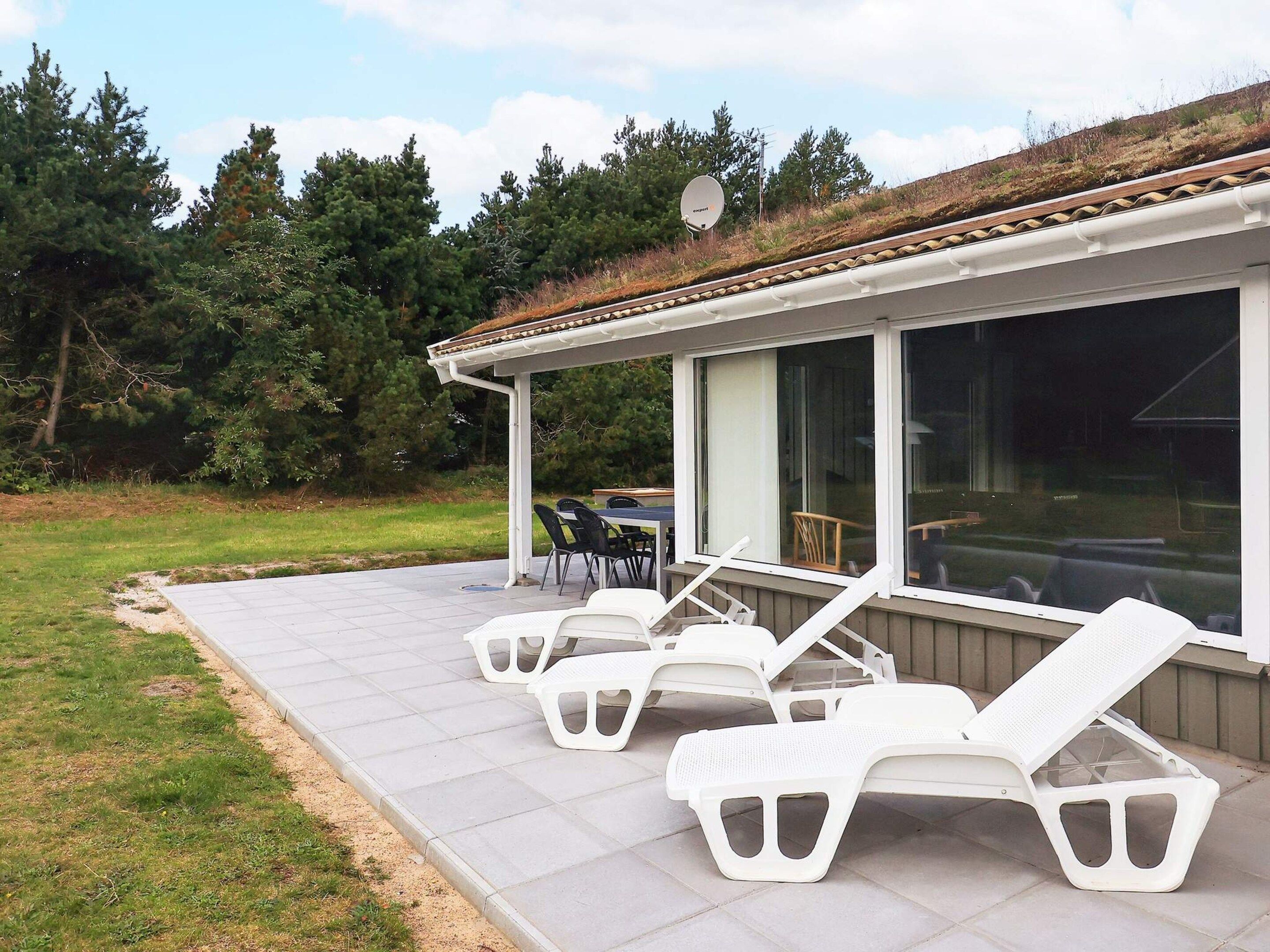Un espacio al aire libre cubierto con patio, sillones de descanso y una mesa.