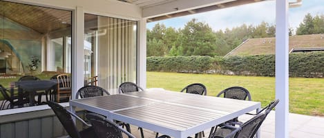 An outdoor patio with a table and chairs, a covered area with a view of a garden and trees.