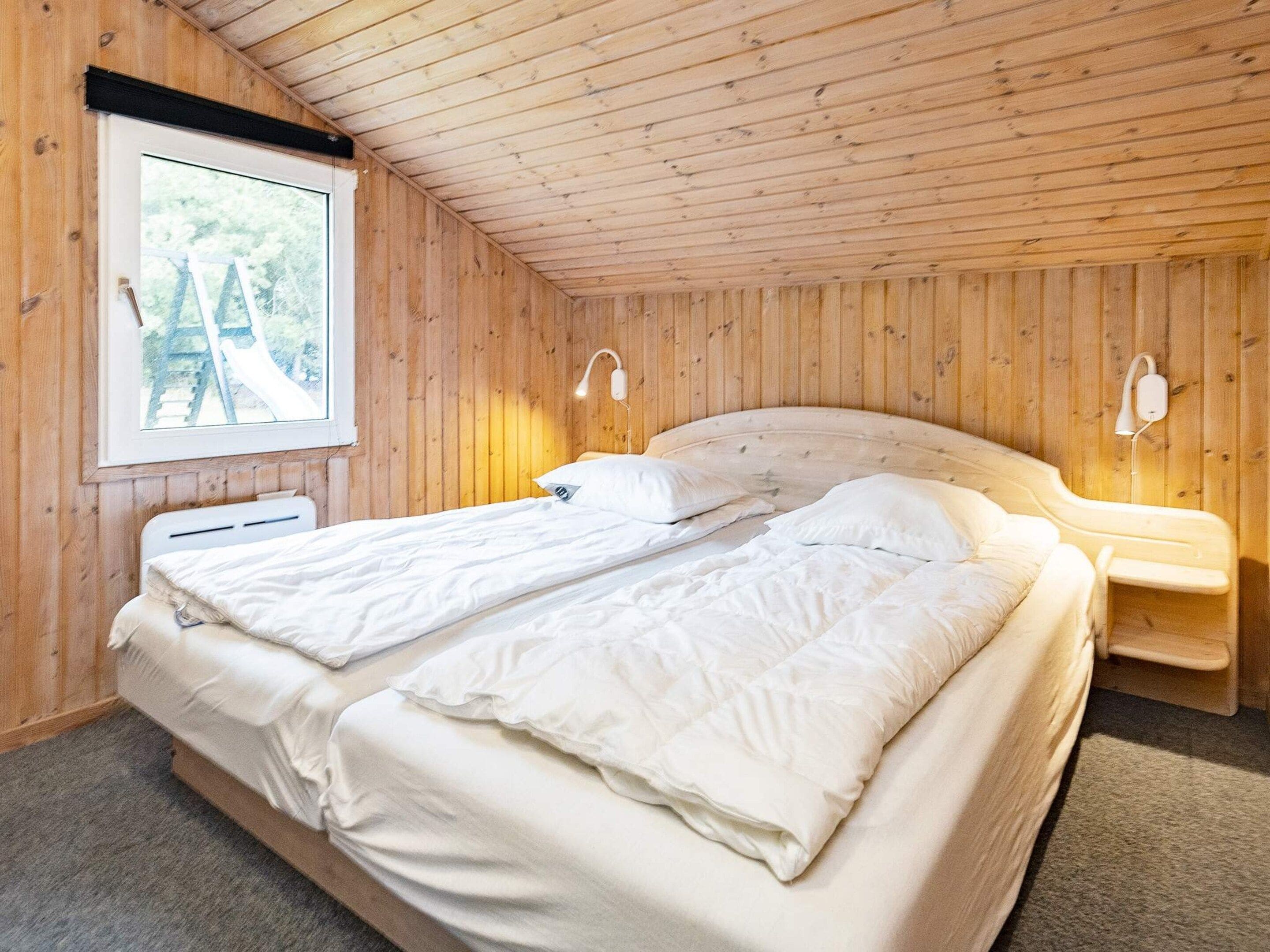 En dobbeltseng med hvide sengetøj i et rum med trævægge og -loft.