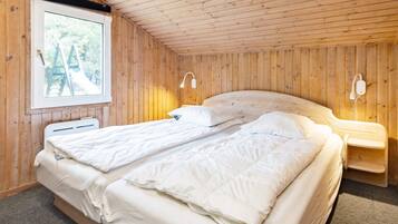 En dobbeltseng med hvide sengetøj i et rum med trævægge og -loft.
