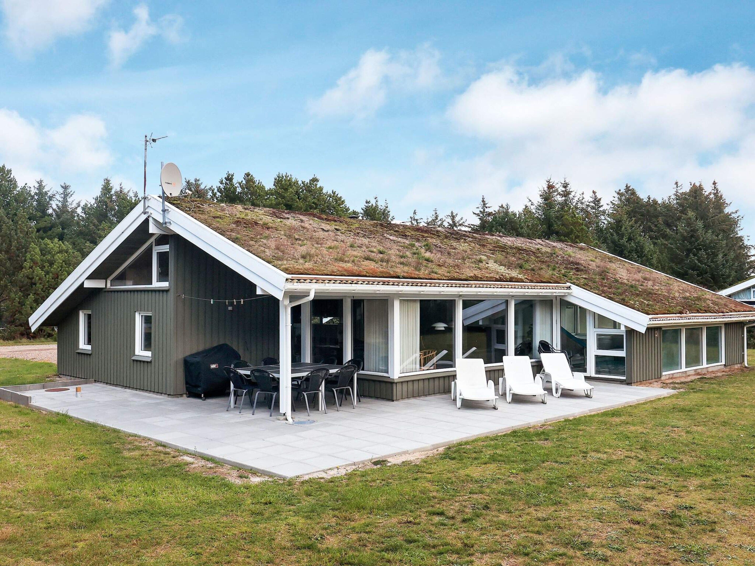 Et moderne hus med saddeltag, en overdækket terrasse med udendørs møbler og en græsplæne.