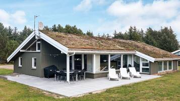 Et moderne hus med saddeltag, en overdækket terrasse med udendørs møbler og en græsplæne.