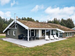 Et moderne hus med saddeltag, en overdækket terrasse med udendørs møbler og en græsplæne.